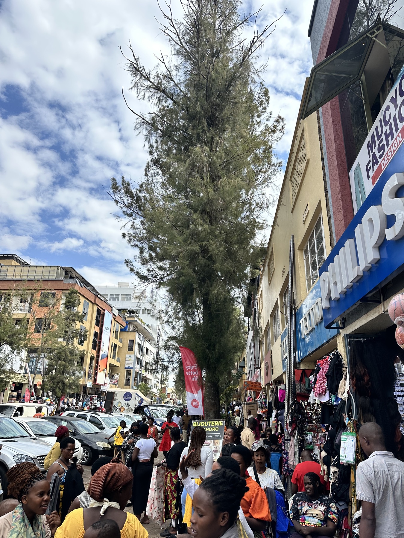 A busy Kigali street market filled with people, cars, storefronts, and layered visual signals